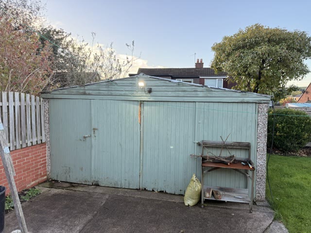 Detached double garage with pale green timber doors and a tired roof