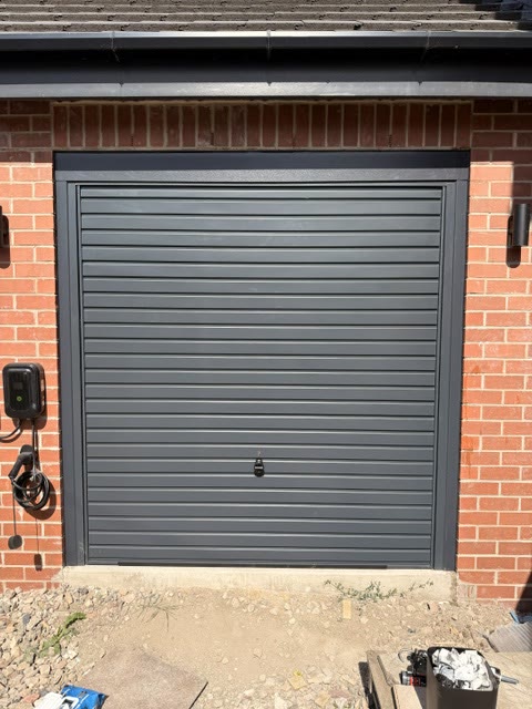 Anthracite insulated roller garage door in a new brick opening beside an EV charger