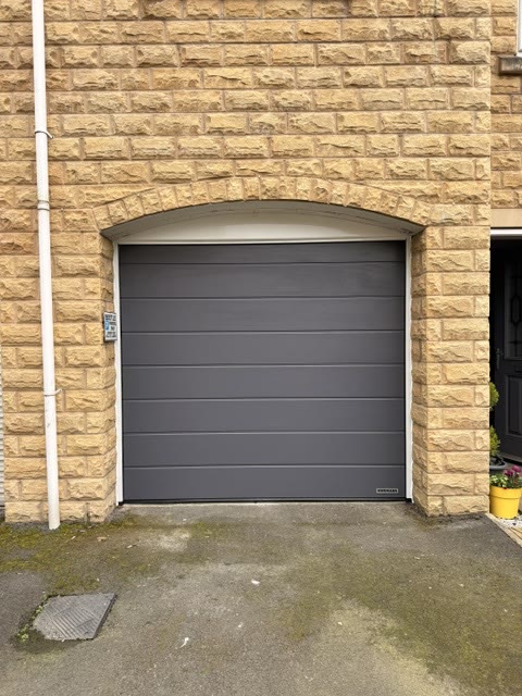 Anthracite sectional garage door fitted into the arched stone opening