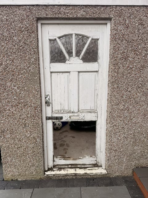 Rotten white timber garage side door with cracked glazing and a decayed threshold