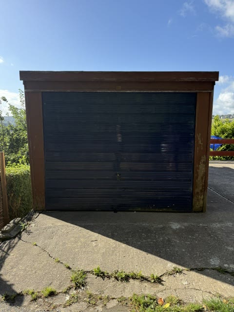 Faded blue up-and-over garage door, rusted at the bottom, in a rotten timber surround